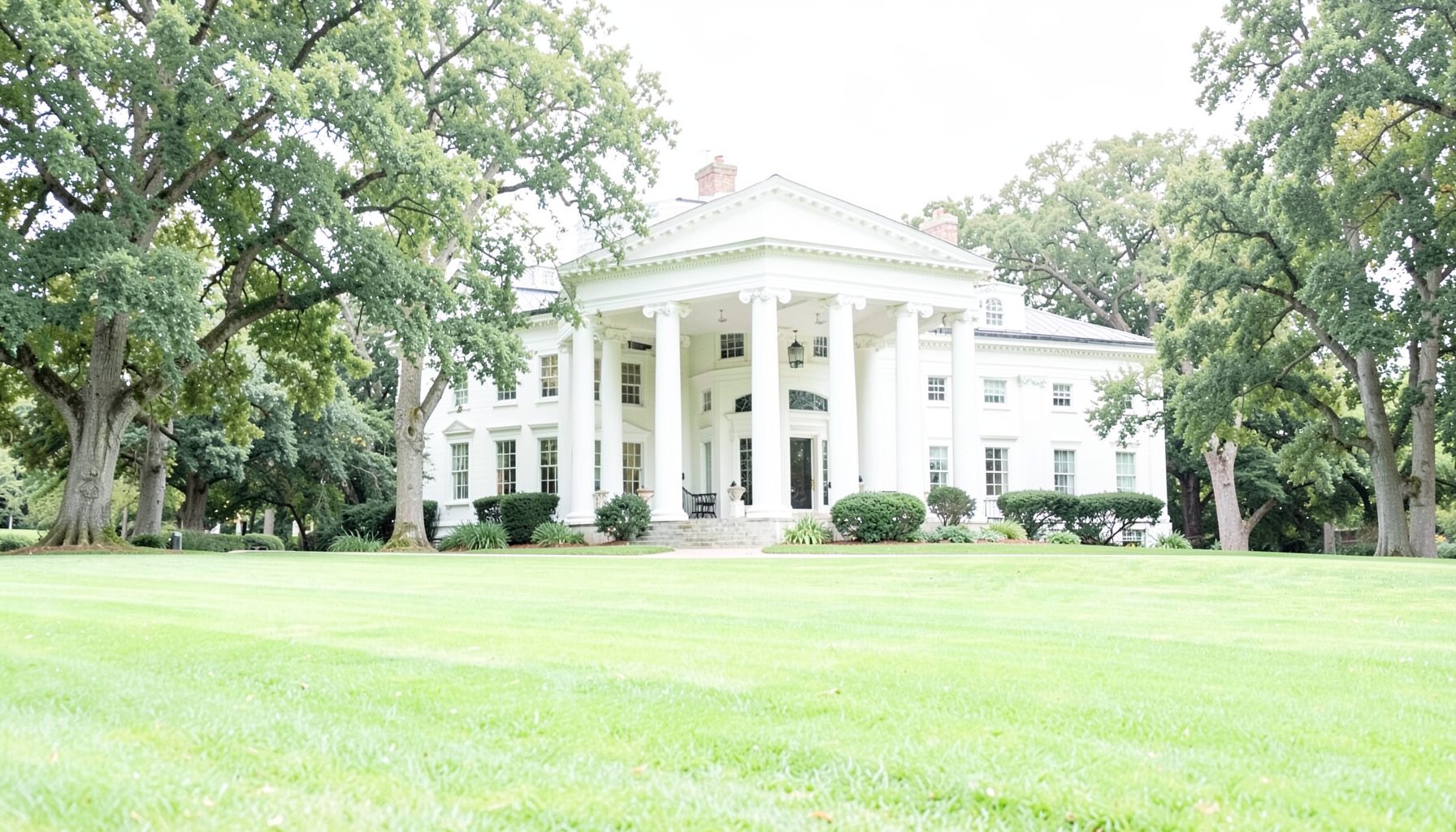 A stately mansion with grand white columns, surrounded by mature trees and a sweeping green lawn