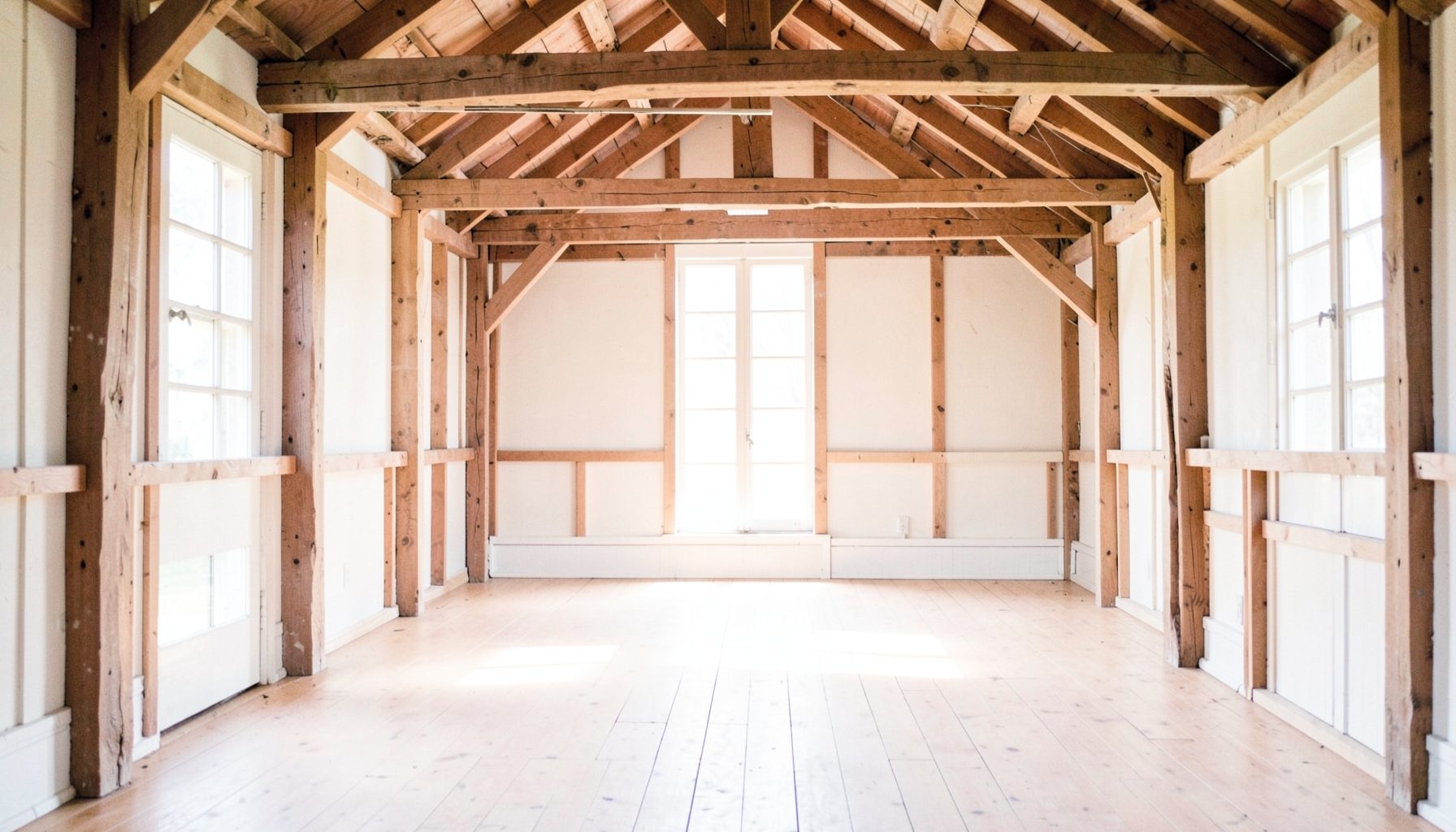 A sunlit rustic barn interior with exposed wooden beams, wide plank floors, and soft natural light streaming through tall windows, creating a warm and romantic atmosphere
